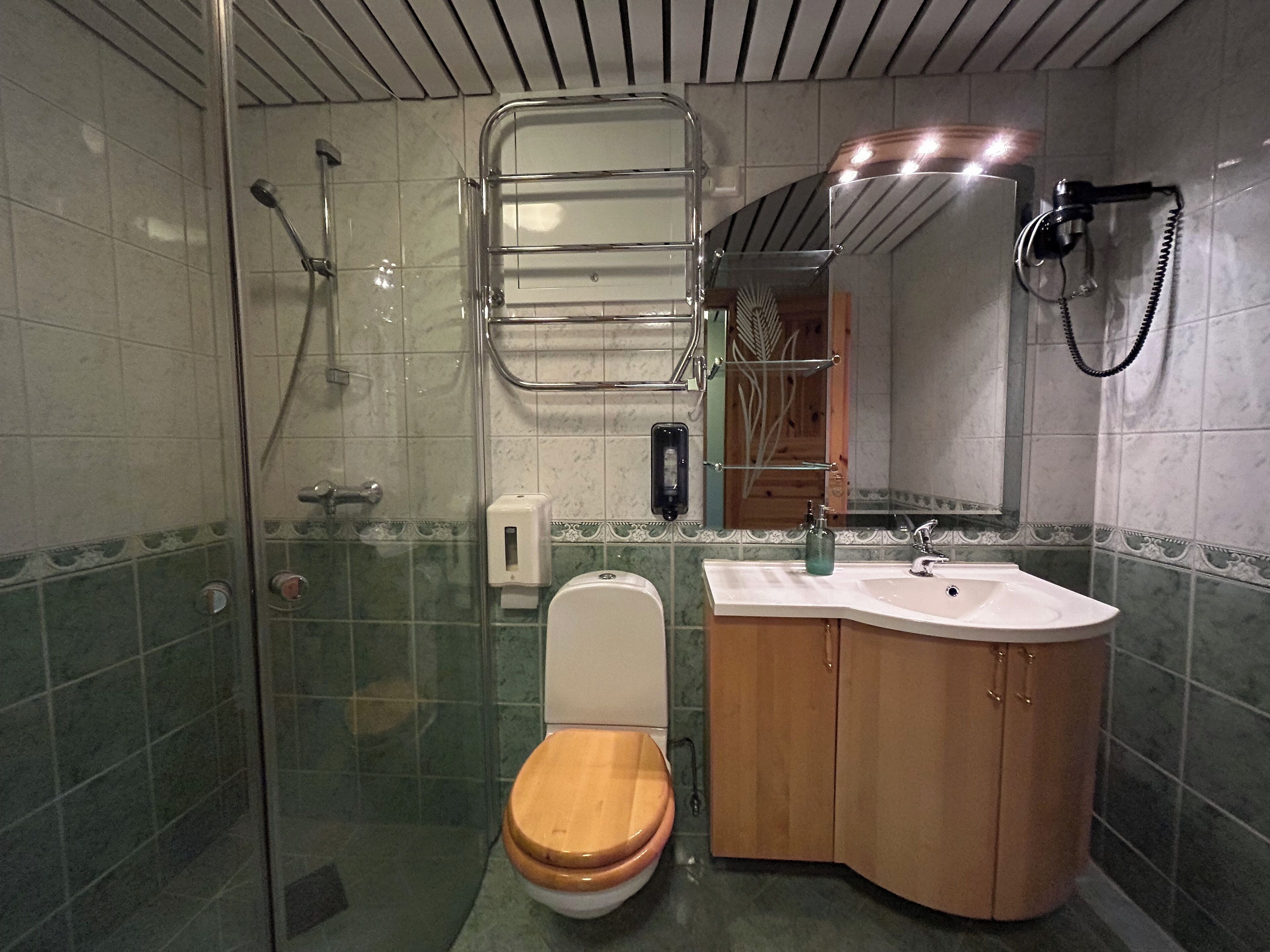 A bathroom with a glass-enclosed shower, a wooden toilet, a sink with a mirror, and a towel rack.