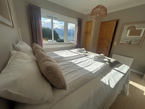 Un dormitorio con una cama grande, una ventana con vistas, una puerta de madera y una lámpara colgante.