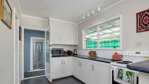A kitchen with white cabinets, a microwave, a kettle, and a stove. - Retro Russell Retreat - Mins to Ferry, Beach, Eats (Russell)