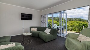 A modern living room with a sectional sofa, a small round table, and a flat-screen TV mounted on the wall. - Retro Russell Retreat - Mins to Ferry, Beach, Eats (Russell)