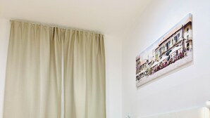 A neatly made bed with a red blanket and white pillows, a wooden floor, and a wall-mounted picture of a street scene. - TAWHID ACCOMODATION (Rome)