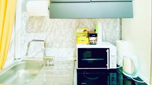 A compact kitchen with a sink, a microwave, and a toaster. There are cabinets above the counter and a towel dispenser. - TAWHID ACCOMODATION (Rome)