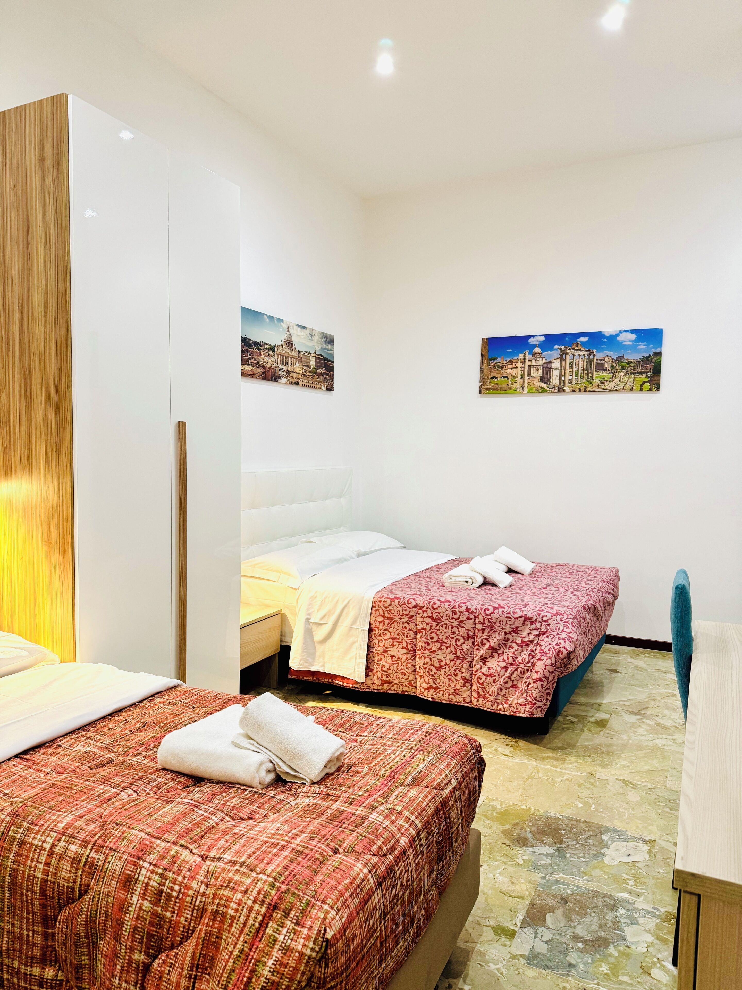 Une chambre d’hôtel avec deux lits, une armoire en bois, un bureau et deux tableaux encadrés au mur.