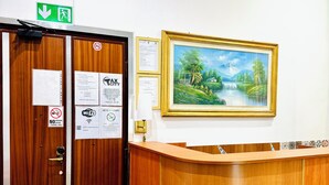 A reception area with a wooden reception desk, a painting of a landscape, and various posted notices including a no-smoking sign and Wi-Fi information. - TAWHID ACCOMODATION (Rome)