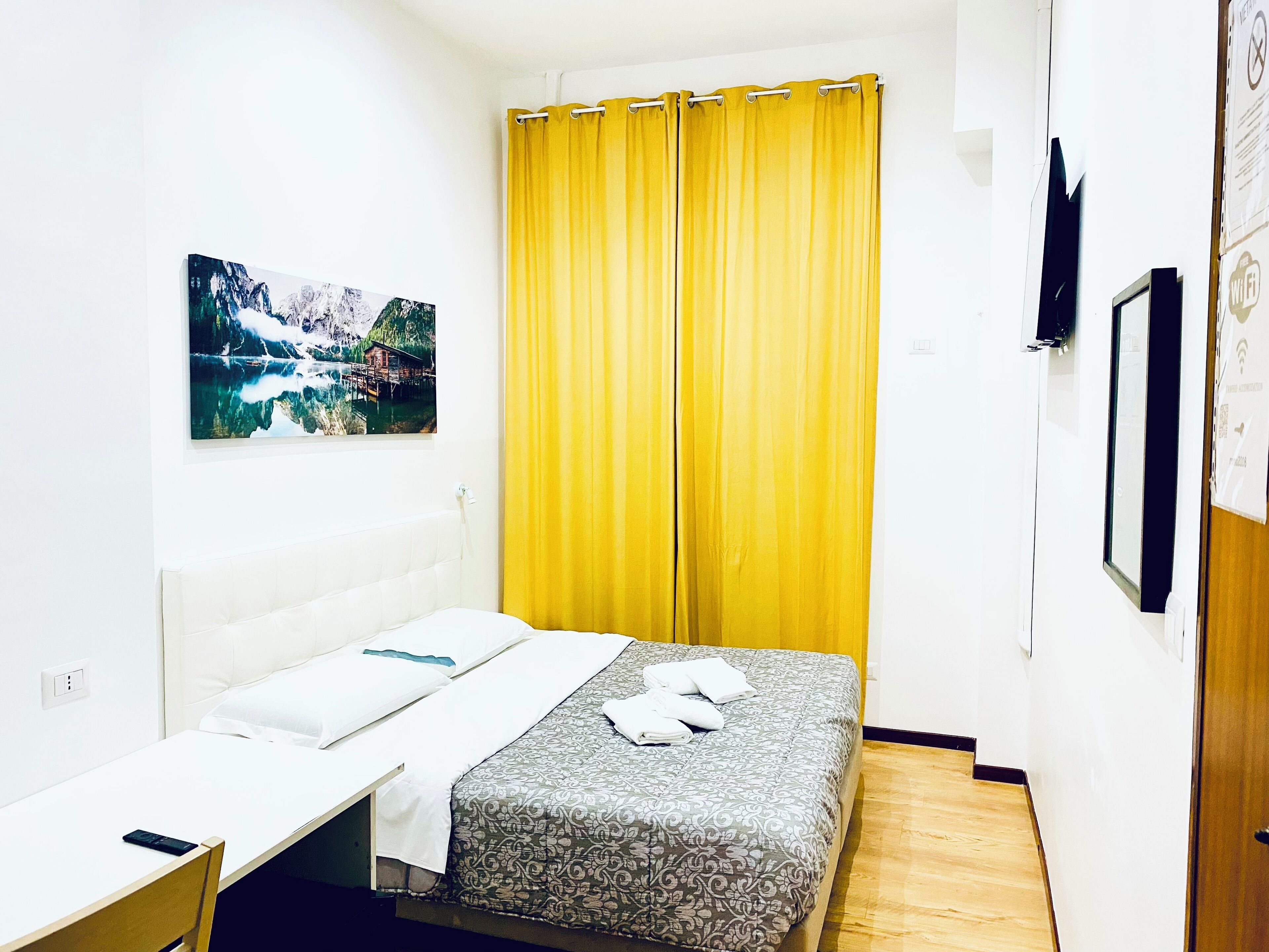 A small, clean room with a bed, a desk, and a yellow curtain.