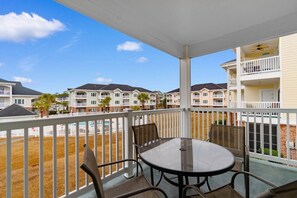 A covered outdoor patio with a table and chairs, overlooking a row of townhouses. - Serene Golf Retreat | Pool, Private Balcony, Grill (Myrtle Beach)