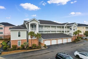 A multi-story hotel with a central courtyard, multiple balconies, and a parking area. - Serene Golf Retreat | Pool, Private Balcony, Grill (Myrtle Beach)