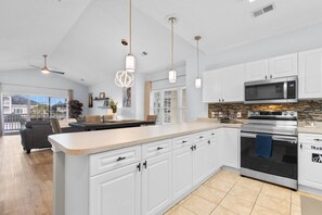 A modern kitchen with white cabinets, a central island, stainless steel appliances, and pendant lighting. - Serene Golf Retreat | Pool, Private Balcony, Grill (Myrtle Beach)