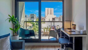 Ein modernes Apartment mit einer großen Schiebeglaswand, einem Schreibtisch mit einem Laptop, einem Stuhl und einem Blumentopf.