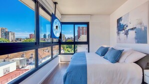 Ein modernes Hotelzimmer mit einem großen Bett, Blick auf die Stadt und einem Wandbild.