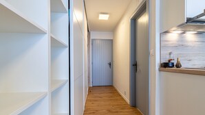 Un couloir étroit avec un plancher en bois, des murs blancs et une porte au fond.