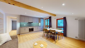 Eine moderne Küche mit grauen Schränken, einem eingebauten Backofen und einem großen Fenster. Es gibt eine Essecke mit Tisch und Stühlen sowie einen runden Couchtisch mit Tassen.
