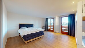 Une chambre à coucher avec un lit, un plancher en bois, une fenêtre avec des rideaux et une vue sur l’extérieur.