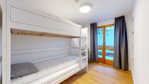 Ein Schlafzimmer mit Etagenbetten, Holzboden, einem Fenster mit Vorhängen und einer Heizung.