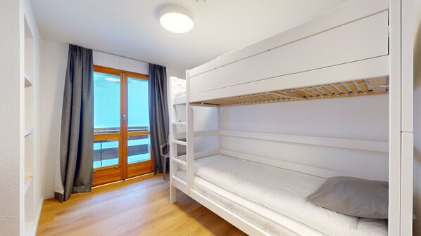 A bunk bed room with a wooden floor, a balcony with a wooden railing, and a sliding glass door.