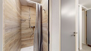 Ein modernes Badezimmer mit Holzvertäfelung, einer Dusche mit Handbrause und einer Tür mit silbernem Griff.