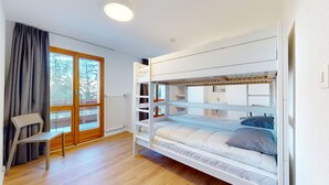 Una stanza con un letto a castello, una sedia, un termosifone e una finestra con tende.