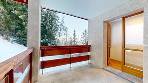 Un balcone con ringhiera in legno, pavimento in cemento e vista su alberi innevati.