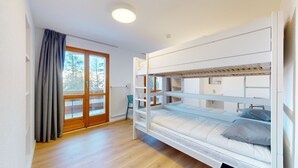 Une chambre avec un lit superposé, un plancher en bois, une fenêtre avec des rideaux et un radiateur.