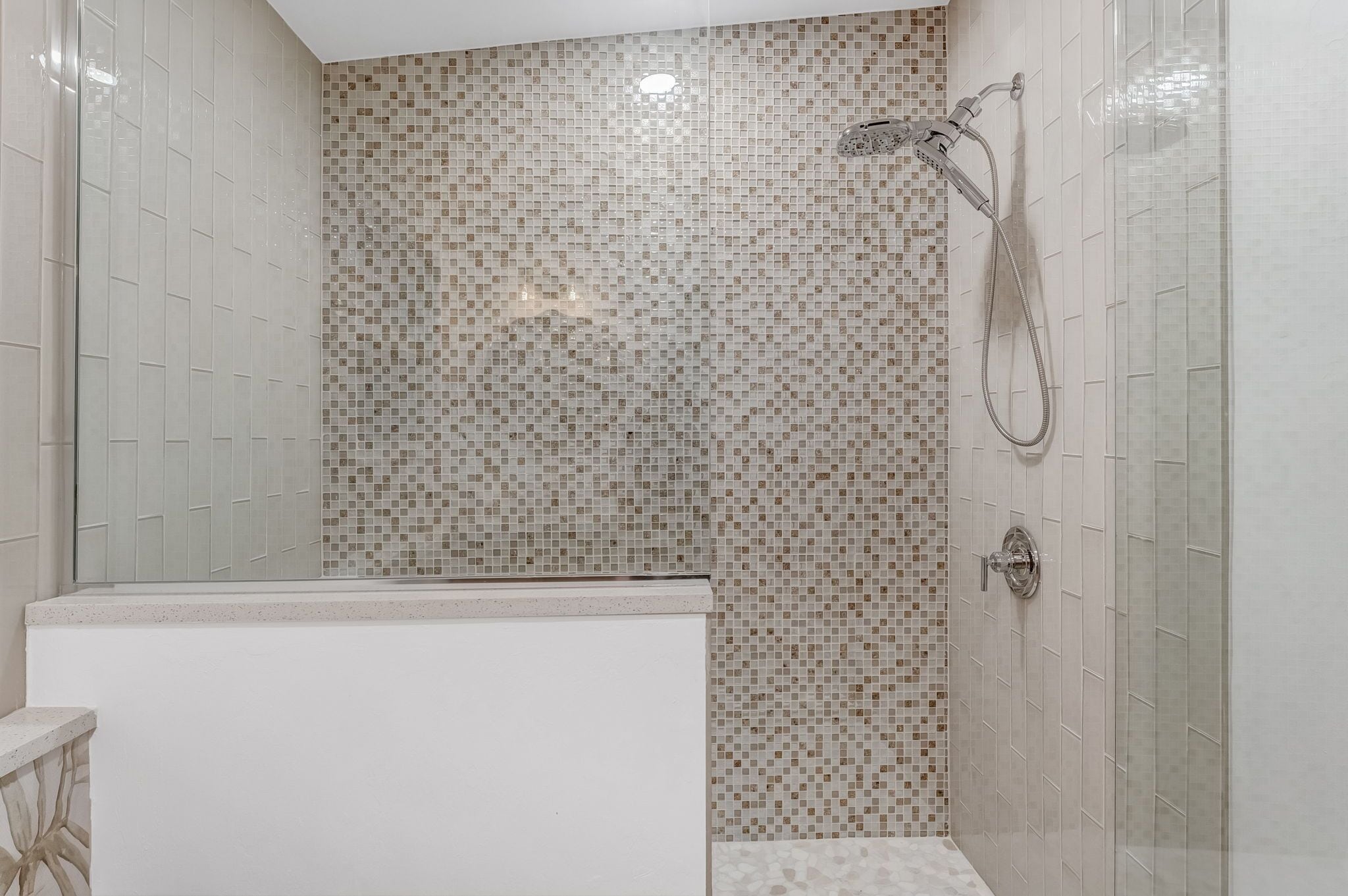 A shower area with mosaic tile walls and a white bathtub.