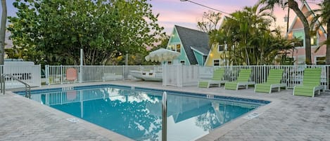 Une piscine entourée d’une clôture blanche, avec des chaises longues vertes et une maison en arrière-plan.