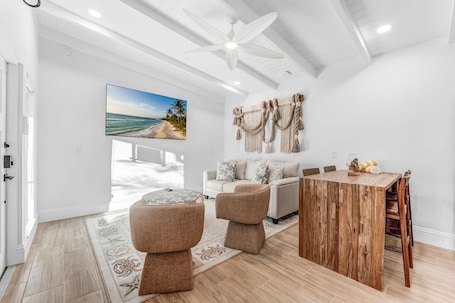 A modern living room with a white sofa, a wooden dining table, and a large painting of a beach scene.. The Anchor Inn