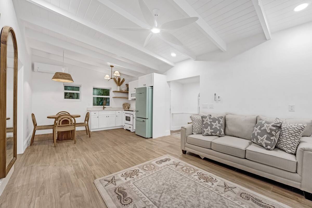 A spacious living area with a beige sofa, a wooden dining table, and a kitchen in the background.