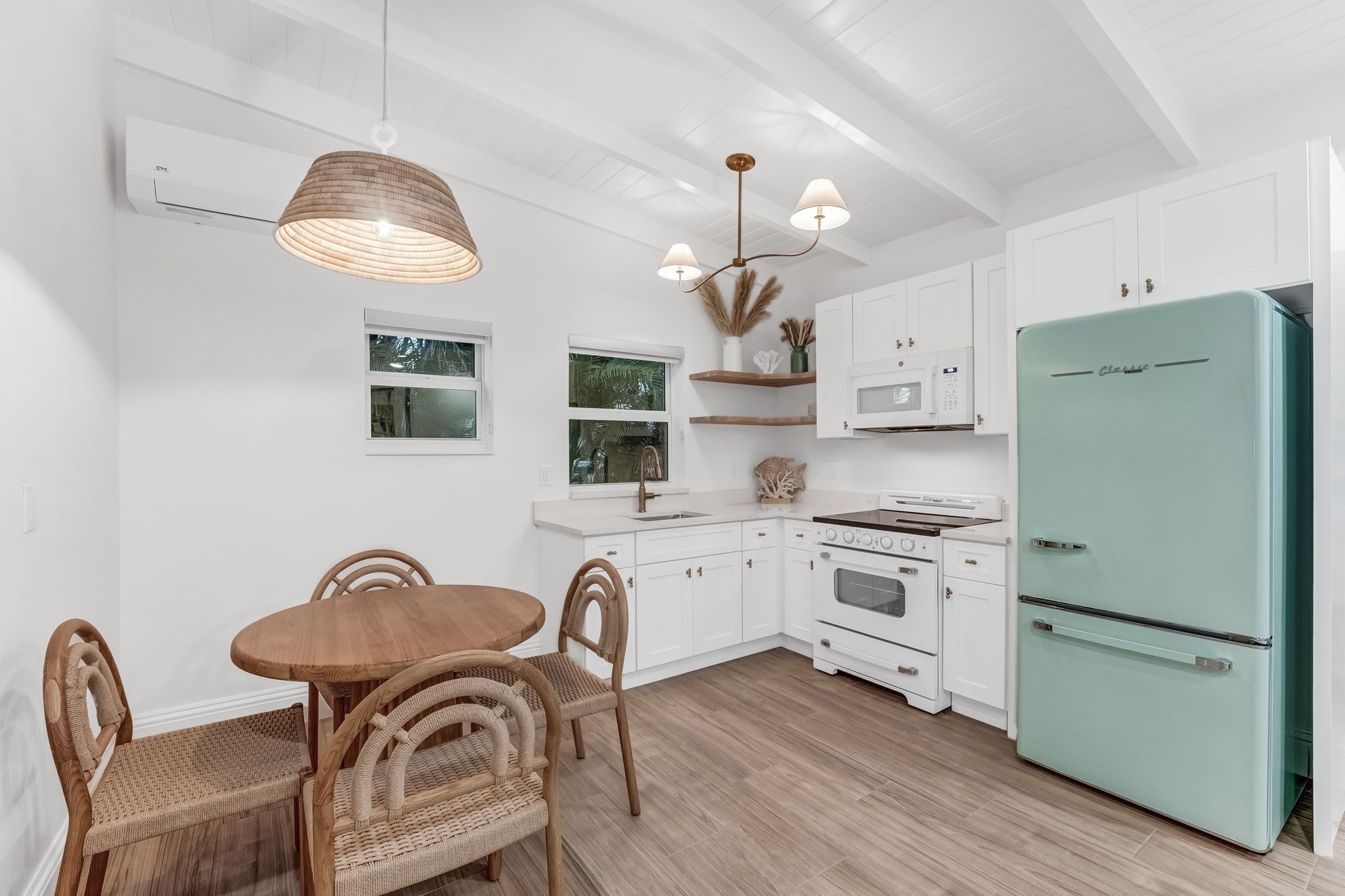 A modern kitchen with white cabinetry, a teal refrigerator, and a dining area with wicker chairs and a wooden table.