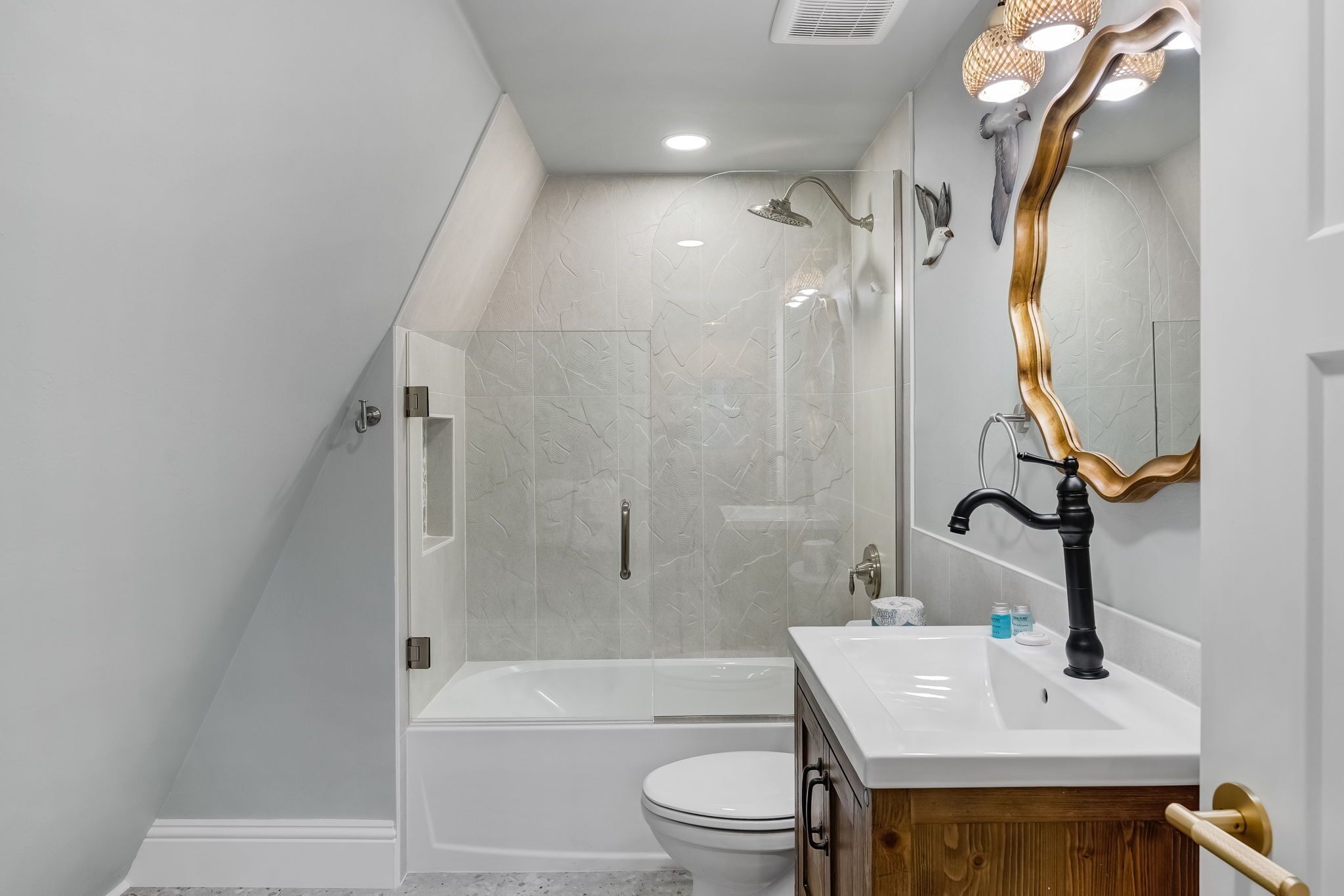Un baño moderno con ducha envuelta en vidrio, una bañera blanca, un inodoro blanco y un tocador de madera con lavamanos blanco.