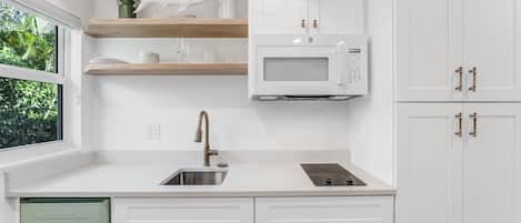 A modern kitchen with white cabinets, a built-in microwave, and a window with a view of greenery.