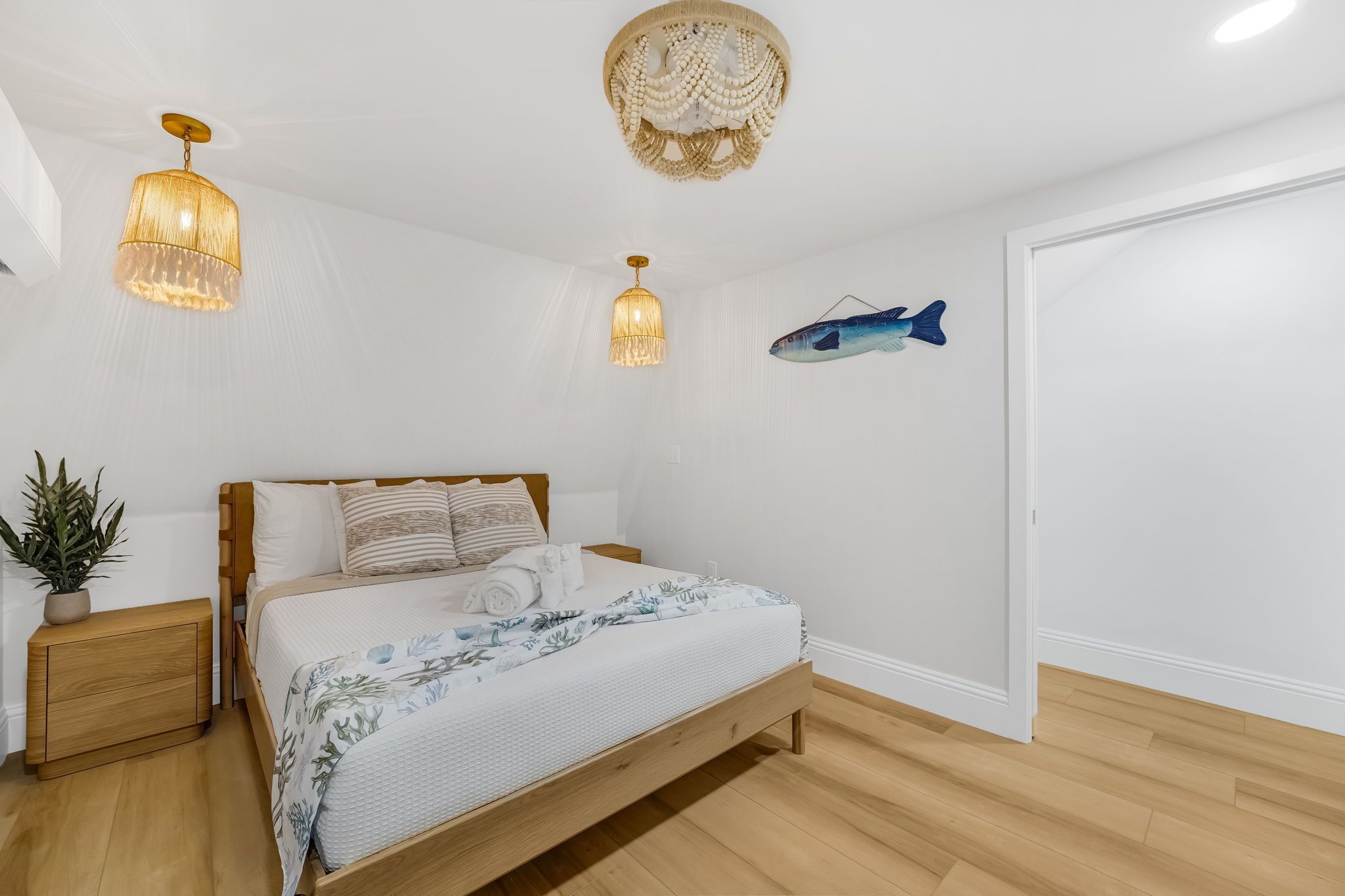 A bedroom with a wooden bed, two bedside lamps, a potted plant, and a fish wall art.