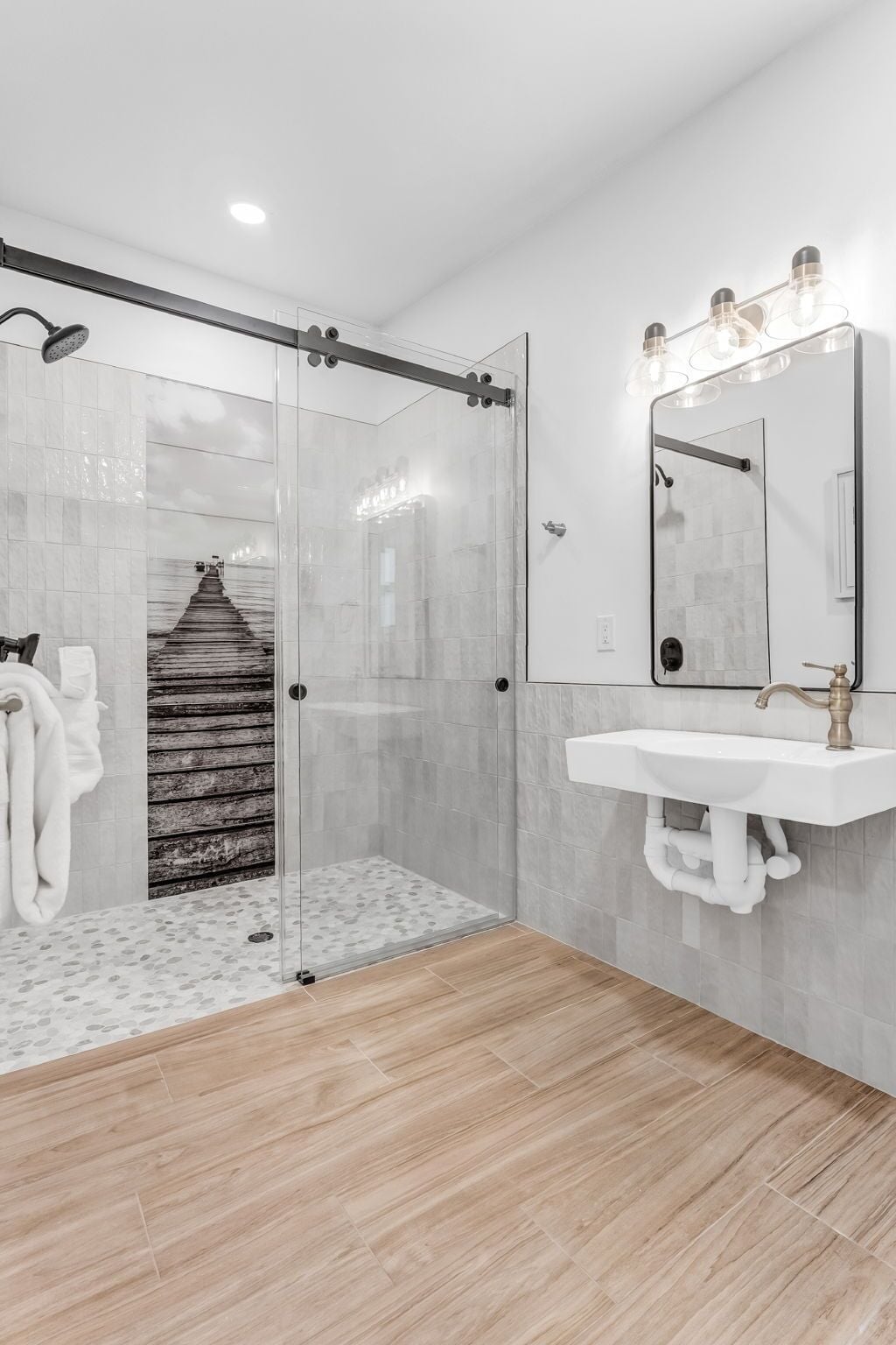 Un baño moderno con cabina de ducha de vidrio, pared decorativa de madera, lavamanos blanco con espejo y un perchero para toallas.