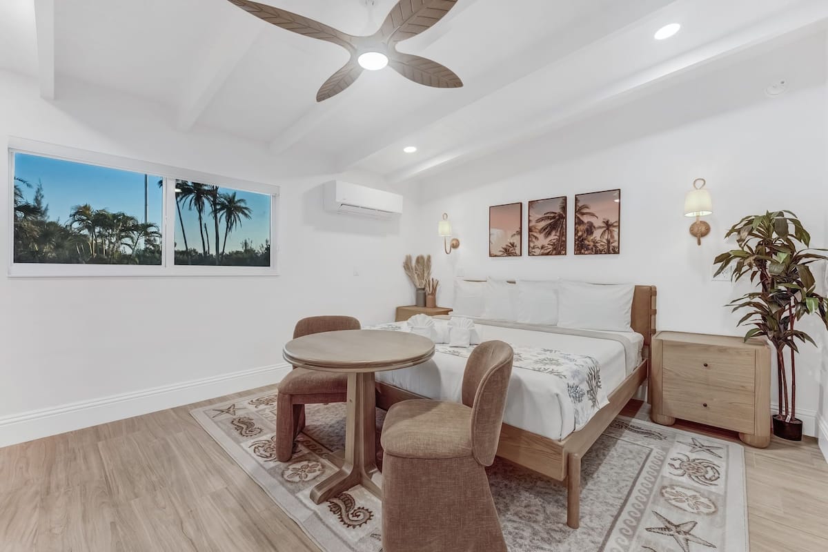 A bedroom with a bed, a round table with chairs, a ceiling fan, and wall-mounted air conditioning.