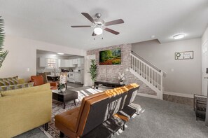 A modern living room with a sofa, coffee table, and a fireplace. There is a staircase leading to another level, and a kitchen in the background. - Modern and Comfy 3BR 2Bath Townhome, near Greenville Downtown  (Greenville)