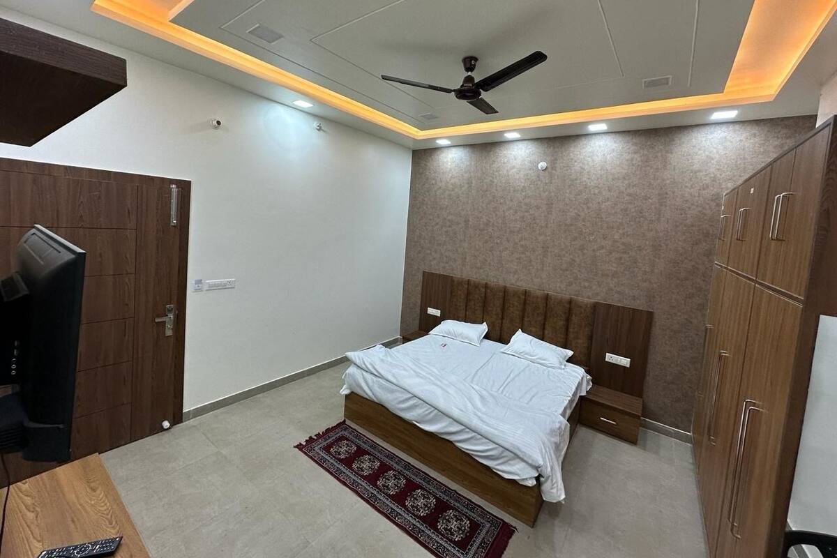A modern bedroom with a bed, wooden wardrobe, ceiling fan, and a TV.