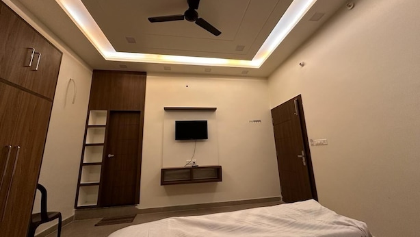 A bedroom with a bed, a ceiling fan, a TV mounted on the wall, and a wardrobe.