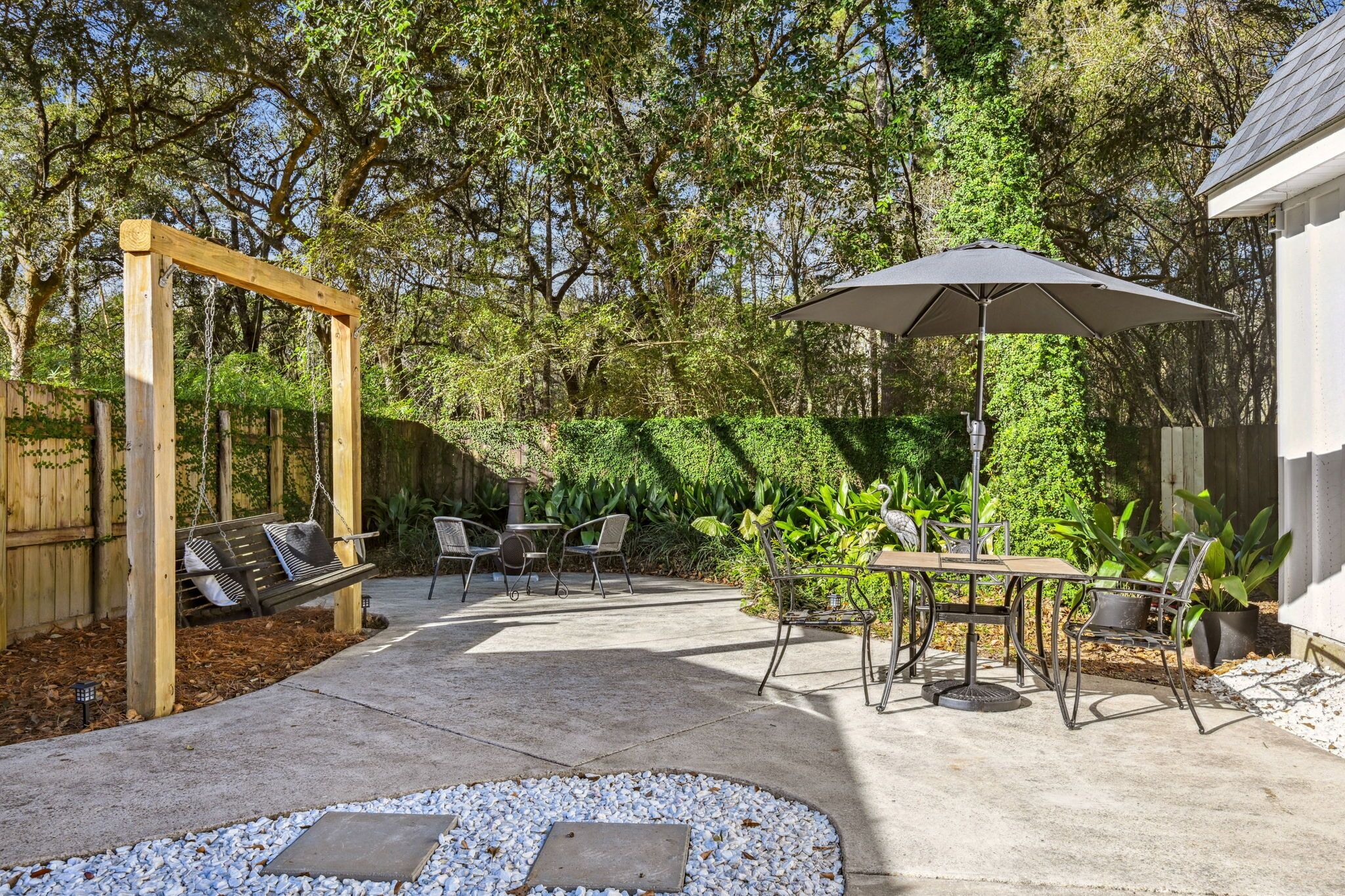 A backyard patio with a swing set, a table with chairs, and a large umbrella.