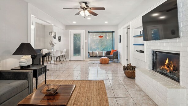 A modern living room with a fireplace, a ceiling fan, and a large TV mounted on the wall. - Perfect Pair: A Peaceful Cottage Vibe & Your Own Private Gameroom. (Covington)