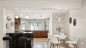 A modern kitchen with a central island, bar stools, a round dining table with chairs, and decorative wall art. - Perfect Pair: A Peaceful Cottage Vibe & Your Own Private Gameroom. (Covington)