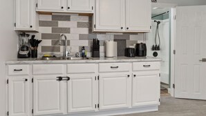 Una cocina moderna con armarios blancos, salpicadero de azulejos y varios electrodomésticos.