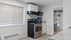 Una cocina compacta con estufa, horno, microondas y armarios blancos.