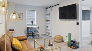 Una sala de estar moderna con un sofá marrón, una mesa de centro de vidrio y un televisor montado en la pared.
