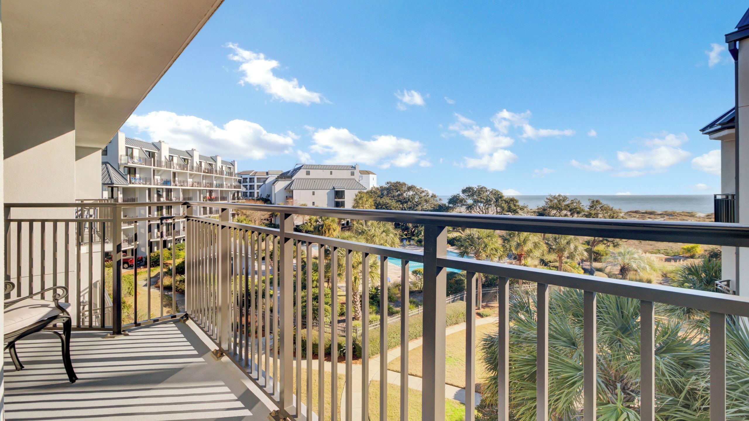Un balcon donnant sur une piscine, un immeuble doté de nombreux balcons et un ciel dégagé.