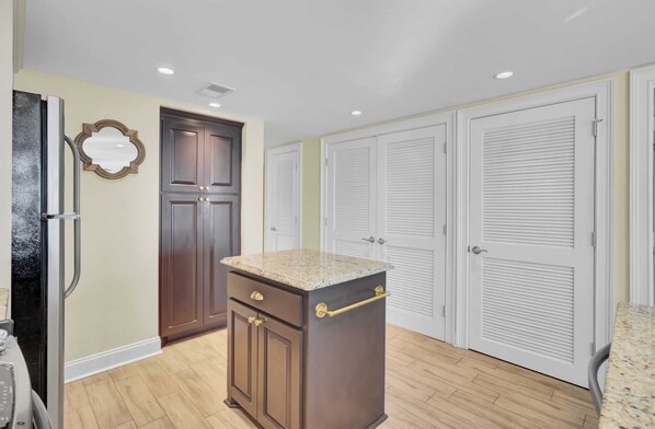 A kitchen with a granite countertop, wooden cabinets, a refrigerator, and white louvered closets.
