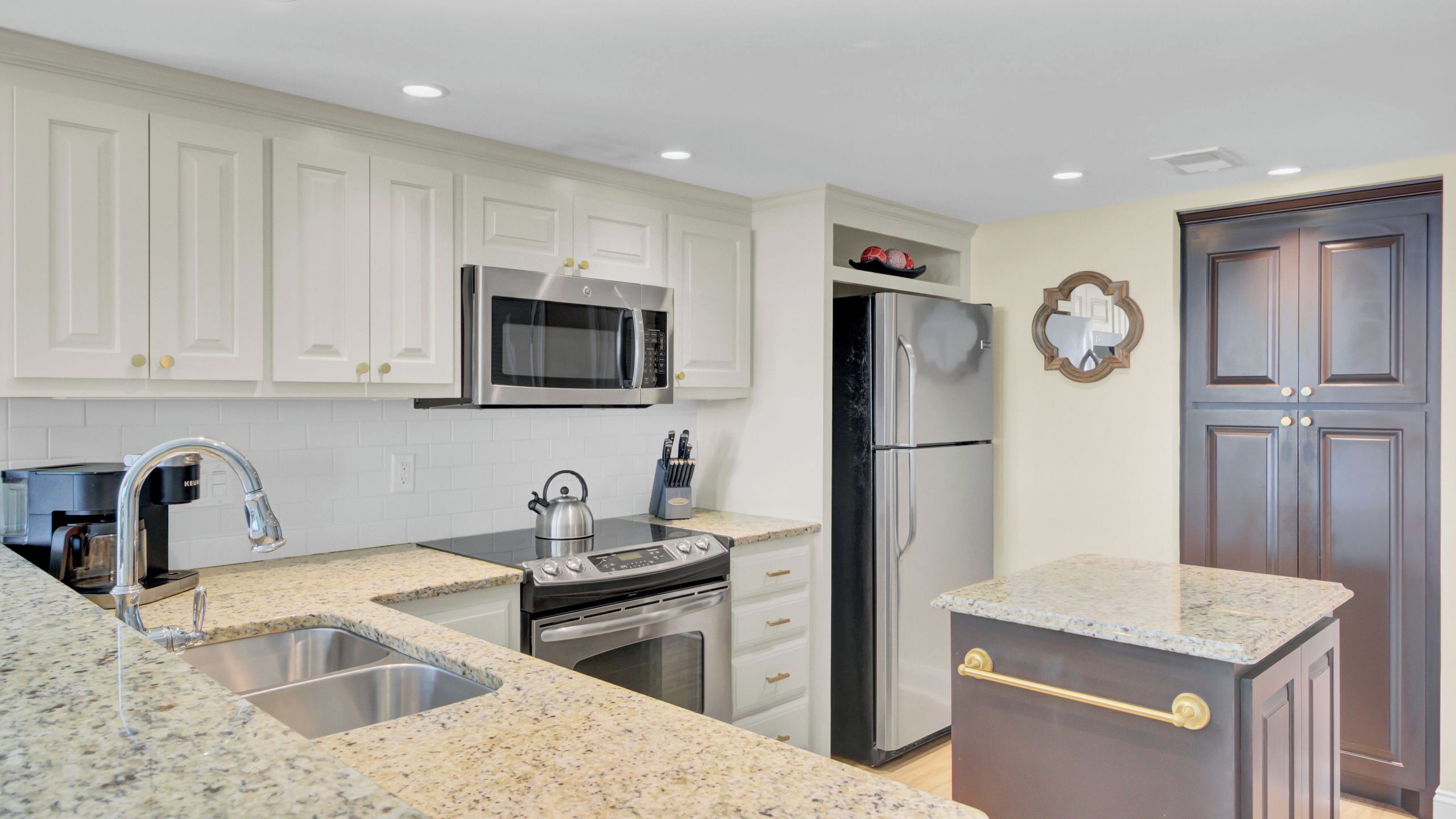 A modern kitchen with white cabinets, stainless steel appliances, granite countertops, and a double door.