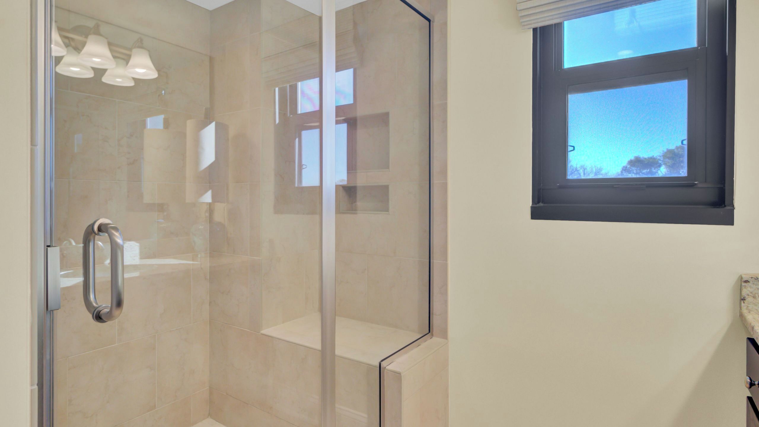 A modern bathroom with a glass shower enclosure, a window with blinds, and a towel rack.