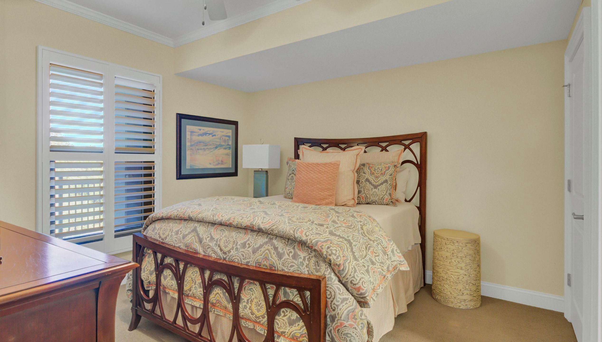 A bedroom with a wooden bed, a nightstand, a lamp, a framed picture on the wall, and a window with blinds.
