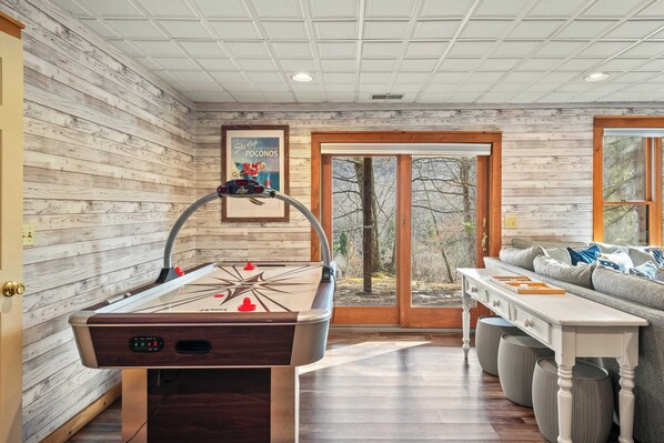 A room with a pool table, a sofa, and a large window with a view of trees.