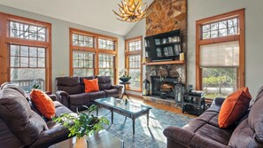 A spacious living room with a stone fireplace, large windows, and leather sofas.