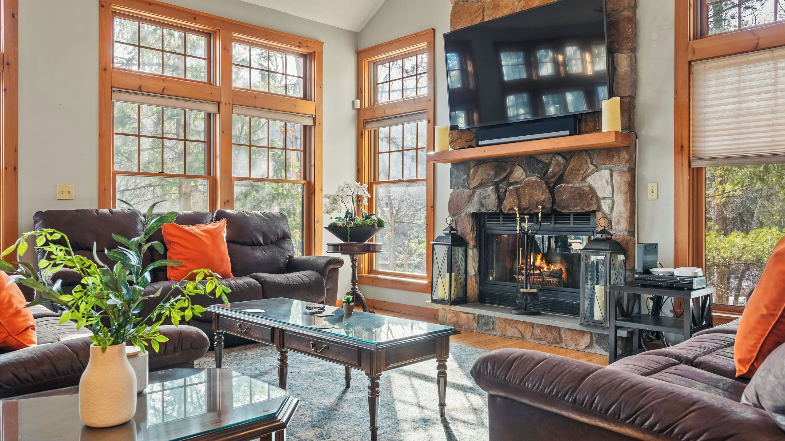 Un salon doté d’une cheminée en pierre, de canapés en cuir et de grandes fenêtres.